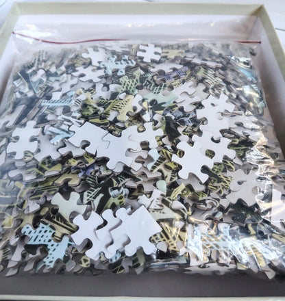 A box of jigsaw puzzle pieces inside a clear plastic bag, showing a multicolor abstract pattern with white puzzle pieces mixed throughout.