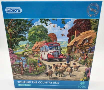 Gibson 1000-piece jigsaw puzzle box titled 'Touring the Countryside' by Steve Crisp, featuring a colorful illustration of a red bus, sheep, country cottages, and people in a rural landscape.