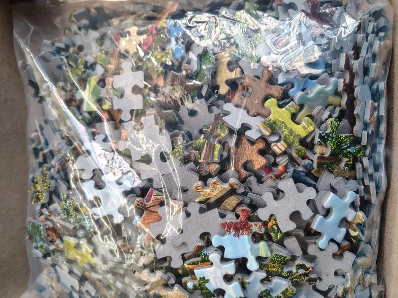 A clear plastic bag filled with assorted jigsaw puzzle pieces featuring various landscape and nature designs, photographed close-up.