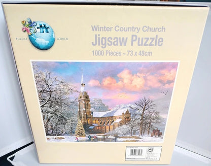 Boxed jigsaw puzzle titled "Winter Country Church" with 1000 pieces, shown against a light gray background. The front of the box features a painted winter scene of a church with snow-covered trees and pink clouds.