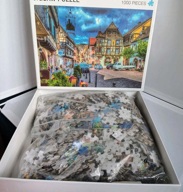 Jigsaw puzzle with a partially completed scene of a town street, displayed in an open box.