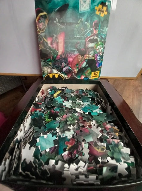Jigsaw puzzle with pieces spilling out of a partially open box featuring superhero graphics.