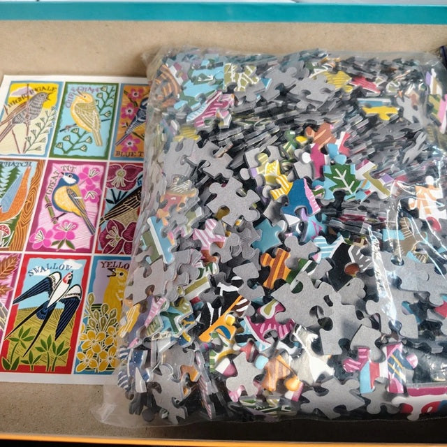 Jigsaw puzzle pieces in a clear bag with colorful bird illustrations on a table.