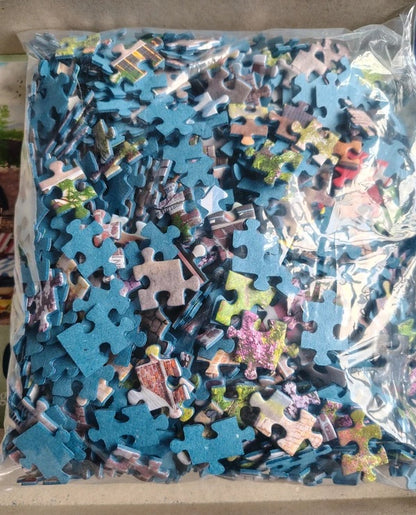A clear plastic bag filled with assorted jigsaw puzzle pieces, many of which are blue, photographed from above on a light beige surface.