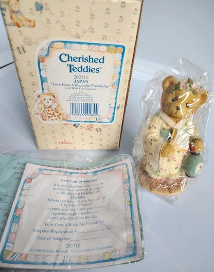 A boxed teddy bear figurine set from Cherished Teddy's, featuring a packaged teddy bear holding a basket and a certificate card, with the branded box standing behind it on a white surface.