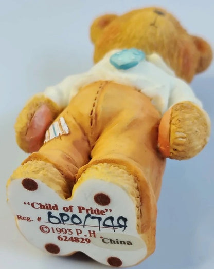 Teddy bear with a heart-shaped tag displaying 'Child of Pride' and production details on a light gray background.