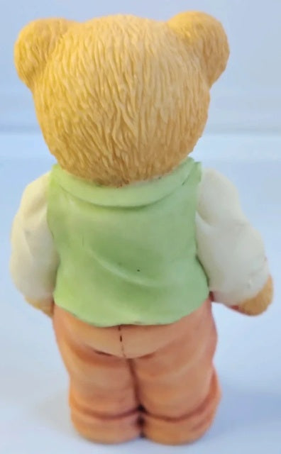 Back view of a teddy bear wearing a green shirt and orange pants on a white background