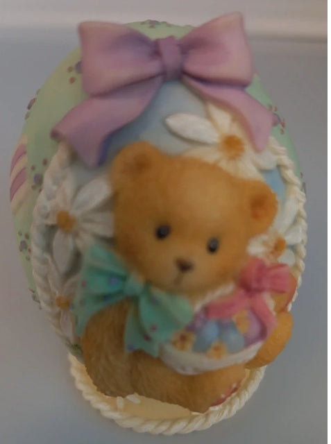 Decorative item with a teddy bear, flowers, and a bow on a pastel background
