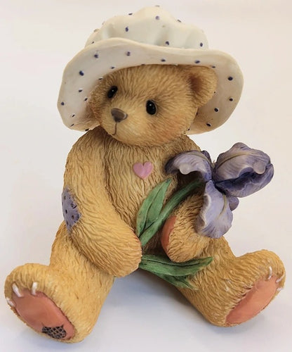 Cherished Teddies Iris teddy bear wearing a hat with a flower and heart design on a white background