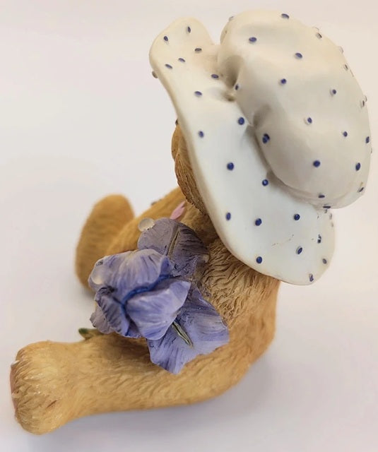 Bear figurine wearing a polka dot hat and holding a purple flower on a white background