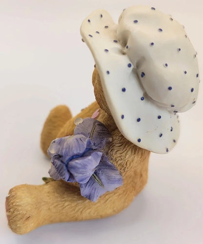 Bear figurine wearing a polka dot hat and holding a purple flower on a white background