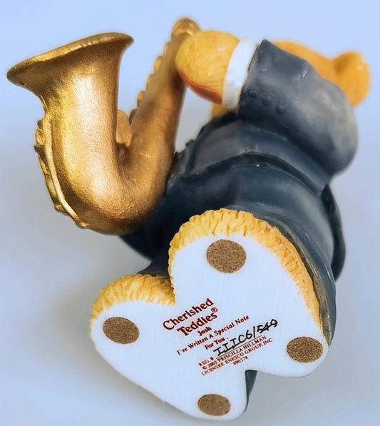 Cherished Teddies Josh playing a saxophone with a heart-shaped tag on a white background