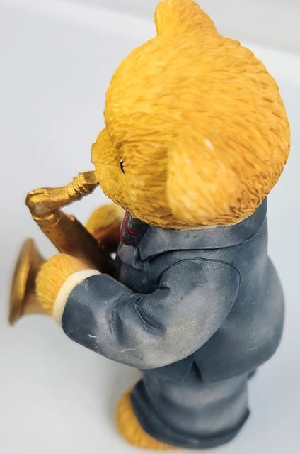 Figurine of a character with a large yellow head and gray suit holding a gold trumpet on a white background