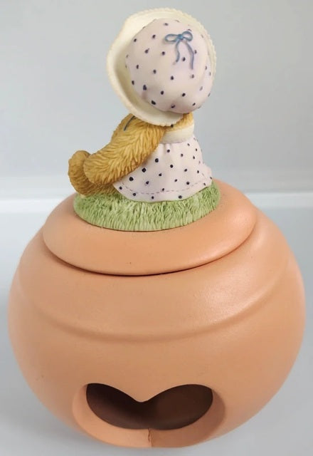 Terracotta pot with a decorative figure on top against a light gray background