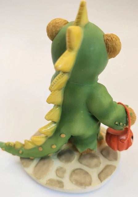 Green dinosaur-like figure with yellow spikes and a red pumpkin on a white background