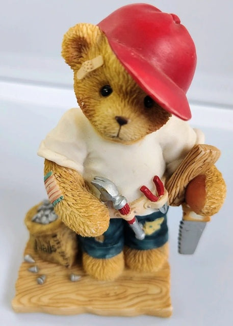 Cherished Teddies Woody Teddy bear figurine wearing a red cap, white shirt, blue shorts, and holding tools on a white background