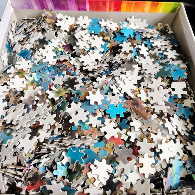 Box of assorted puzzle pieces with a colorful top edge