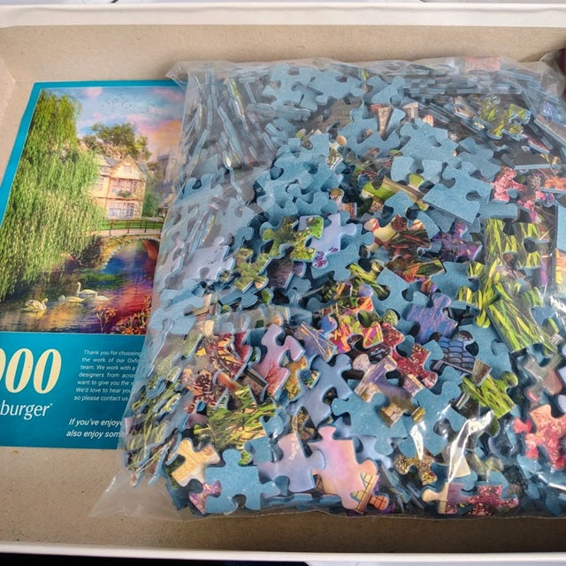 Jigsaw puzzle with pieces partially assembled on a cardboard box, featuring a colorful illustration of a scenic landscape.