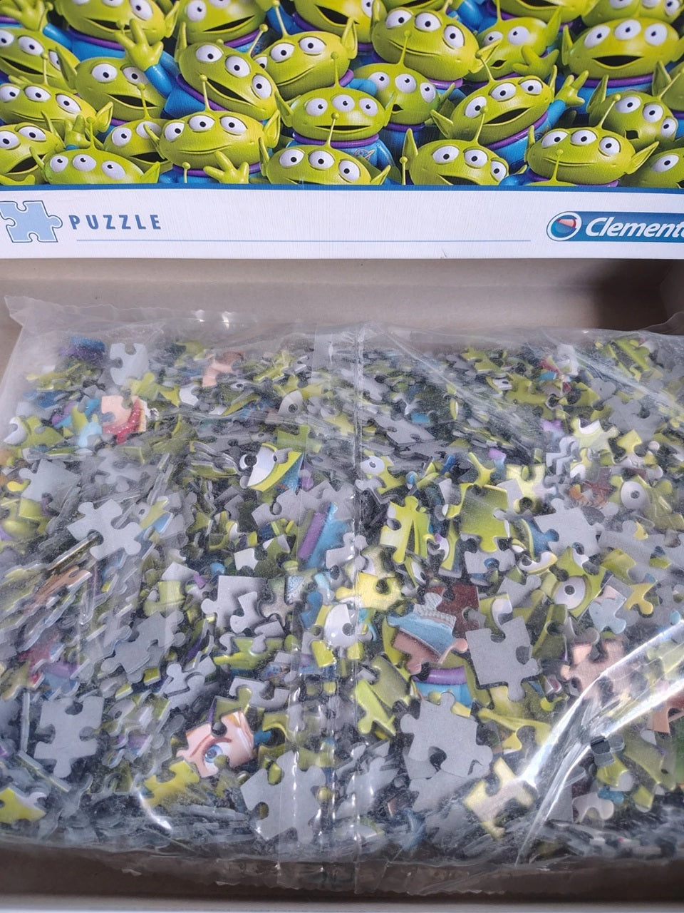 A Clementine brand jigsaw puzzle box showing the green alien character design on the lid and a clear plastic bag filled with puzzle pieces below.