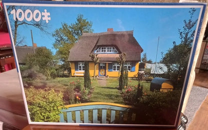 Jigsaw puzzle box with a picture of a thatched-roof house and garden.