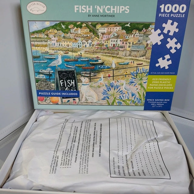 Jigsaw puzzle box for 'Fish 'N' Chips' by Anne Mortimer, showing a coastal scene with houses and boats.