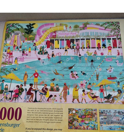 A colourful 1000-piece jigsaw puzzle featuring a lively poolside scene at 'Flamingo Park' with many people swimming, relaxing, and playing near a pink and yellow pavilion. The puzzle is photographed flat on a neutral surface, showing the top puzzle area and a small portion of the lower cardboard backing with text and inset images.