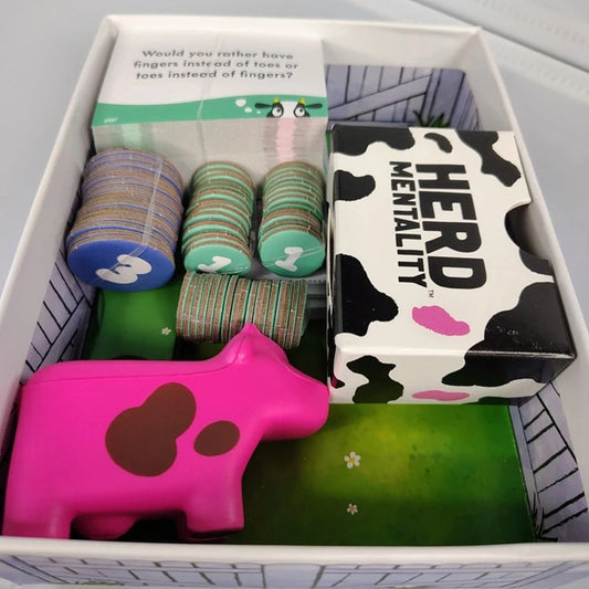 Box containing 'Herd Mentality' game components with cow-themed items.