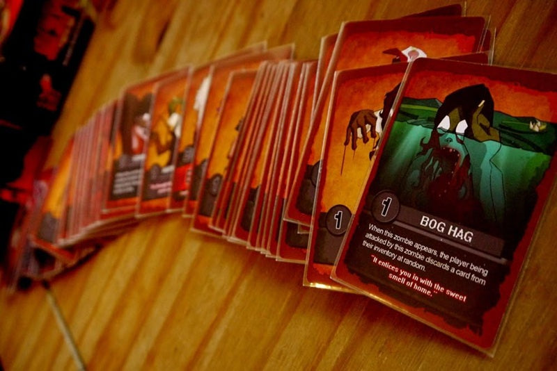 Row of game cards on a wooden surface, with 'Bog Hag' card in focus.