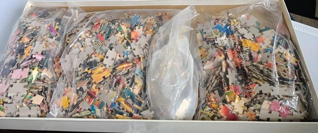 Box of assorted colorful puzzle pieces in clear bags