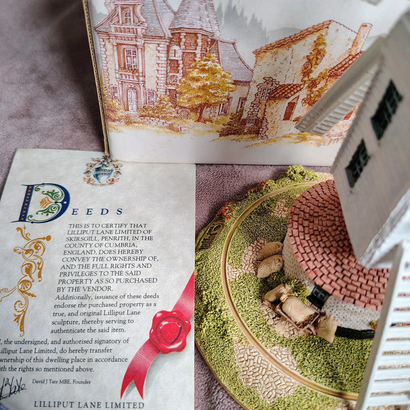 Model of a house on a decorative plate with a piece of paper titled 'Deeds' and an illustration of a house in the background.