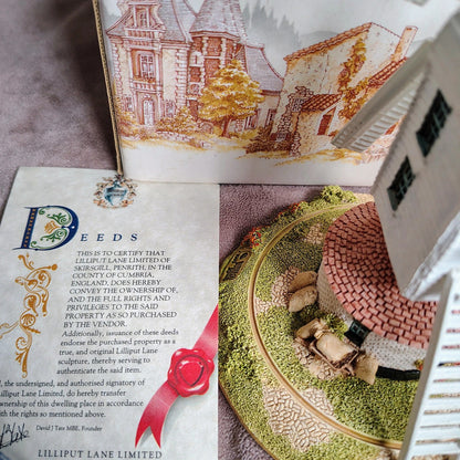 Model of a house on a decorative plate with a piece of paper titled 'Deeds' and an illustration of a house in the background.