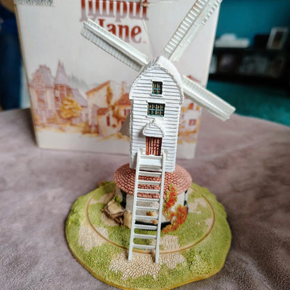 Model windmill on a round base with a book titled 'Upupi Lane' in the background.