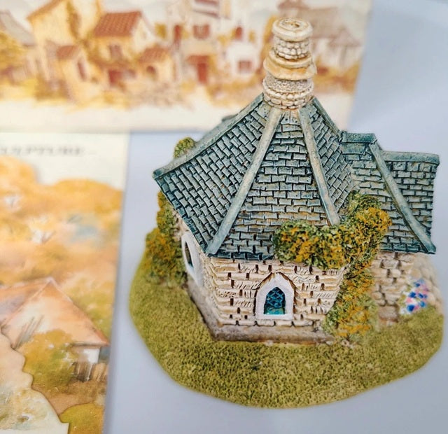 Miniature model of a stone building with a green roof on a textured surface.