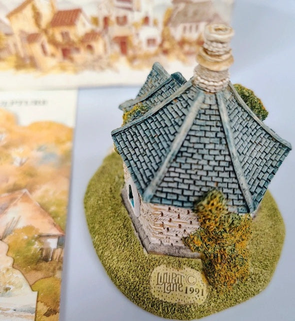 Miniature model of a building with a textured roof and green base, featuring the brand 'Lladró'.