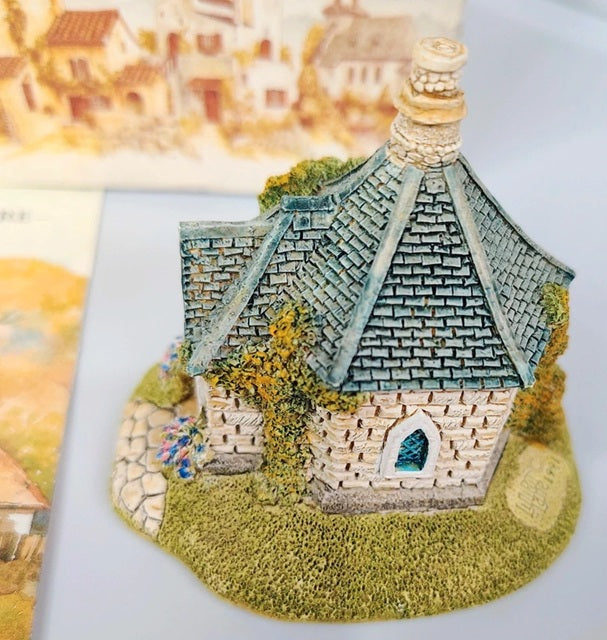 Miniature model of a stone building with a tiled roof on a textured surface.