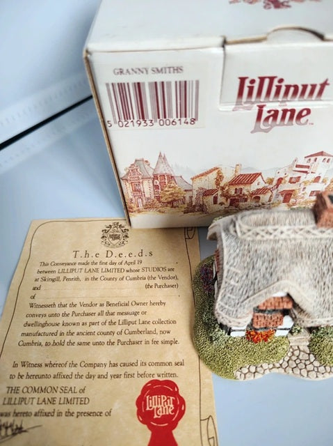 A boxed miniature building set labeled 'Lilliput Lane' with a printed instruction card and a small model town scene on a tabletop.