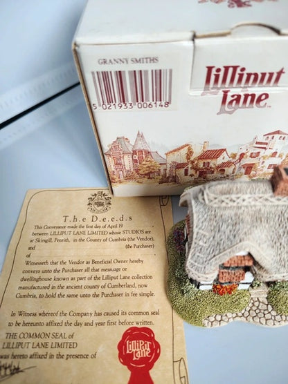A boxed miniature building set labeled 'Lilliput Lane' with a printed instruction card and a small model town scene on a tabletop.