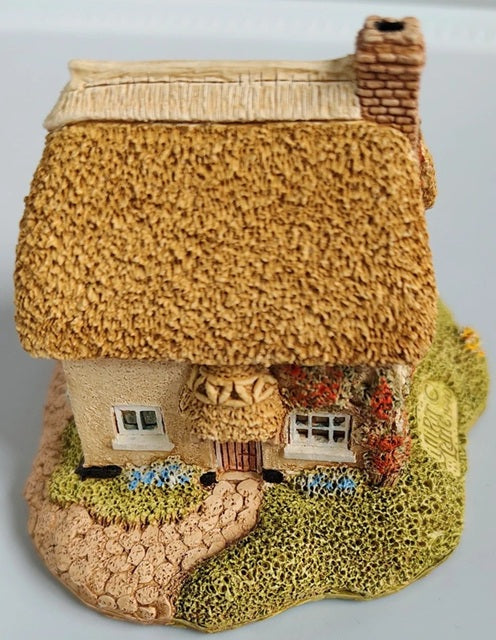 Decorative model of a thatched-roof cottage with garden on a gray background