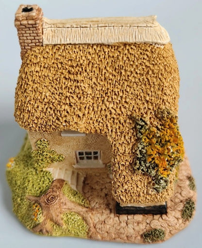 Model of a thatched cottage with textured walls and greenery on a light blue background