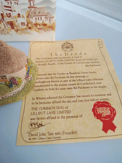 A vintage-style Lilliput Lane Limited deed certificate on aged beige paper, shown alongside a small decorative illustration and a textured object in the background.