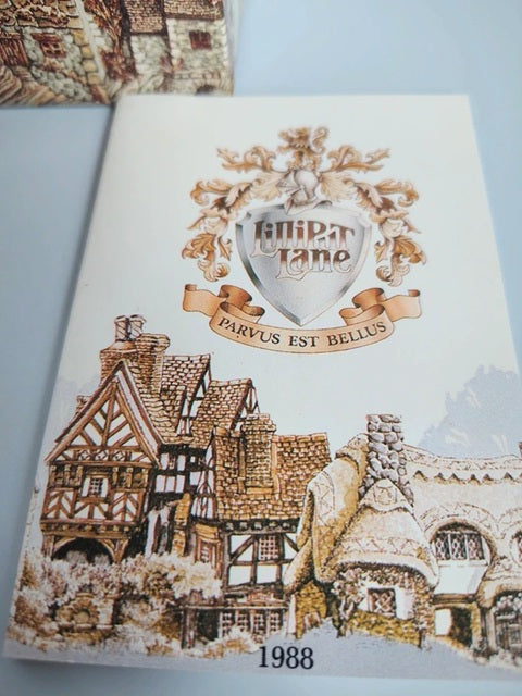 A printed card or booklet cover featuring a cream background with an illustrated village scene in brown, beige, and gray tones. A central crest reads 'Hilpertlano' with the motto 'Parvus est bellus,' and '1988' appears at the bottom.