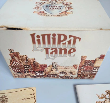 A vintagebox for 'Liliput Lane' featuring an illustration of medieval houses and a crest on the lid, photographed on a light blue surface.
