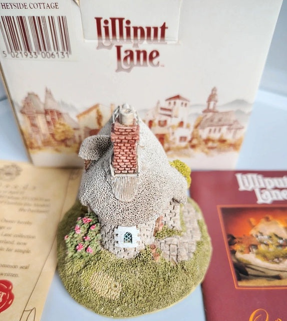 A miniature decorative cottage figurine from Lilliput Lane, displayed in front of its original white packaging box and an instruction booklet.