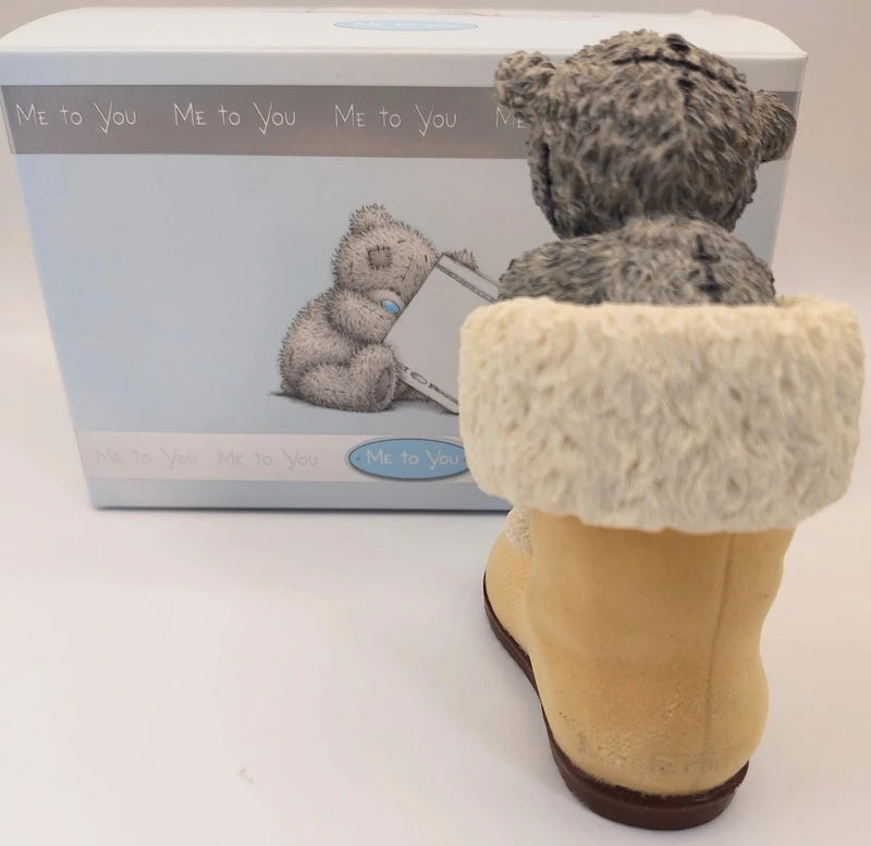 A Me to You teddy bear figurine wearing a beige boot with a white faux-fur trim, shown from the back next to its original light blue packaging box.
