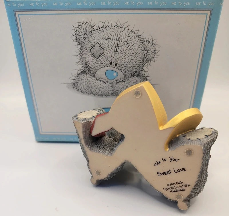 A Me To You 'Sweet Love' teddy bear figurine shown in front of its original light blue packaging box. The figurine is cream-colored with gray textured fur details and a yellow collar.