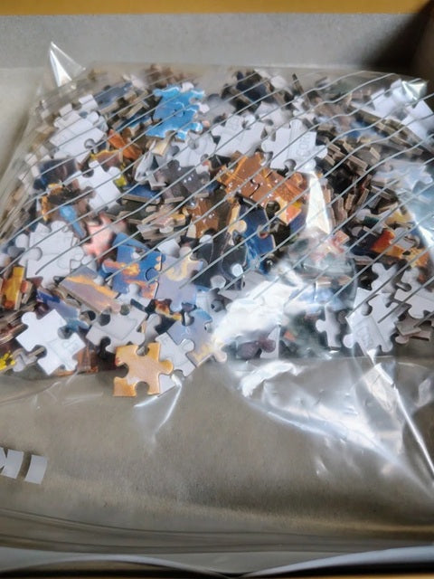 Pile of jigsaw puzzle pieces in a clear plastic bag on a cardboard surface