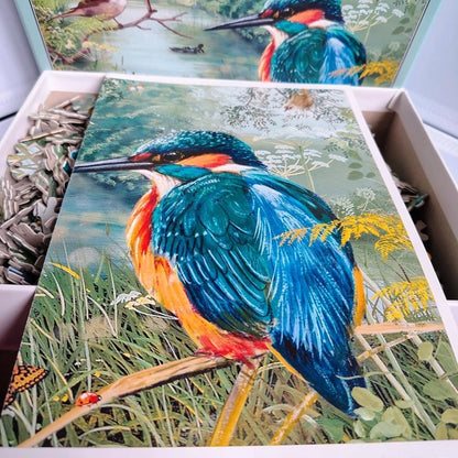 Colorful bird painting on a wooden board with a box of puzzle pieces in the background.