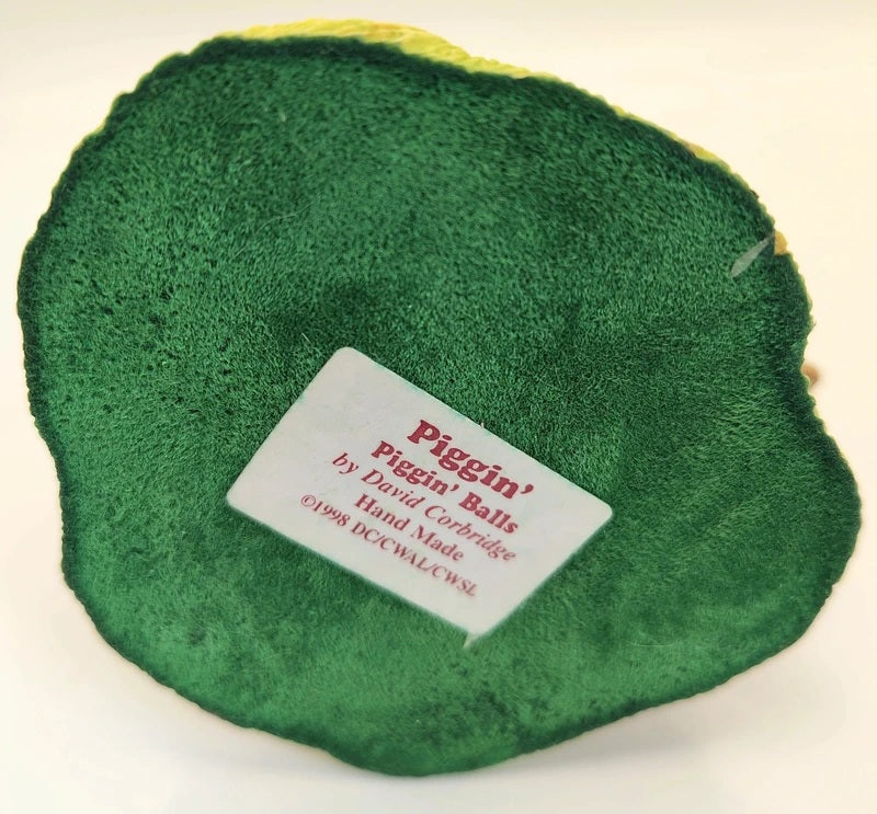 A green textured plush or felt disc with a white paper label reading 'Piggin' Balls by David Corbridge Hand Made 1998 by David Corbridge' on a plain white background.