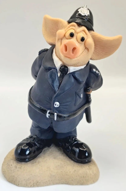 A collectible figurine of a pig dressed in a dark blue police uniform with a black hat, white shirt, and black shoes, standing on a beige rock base against a light gray background. Piggin Policeman PI.G figurine.