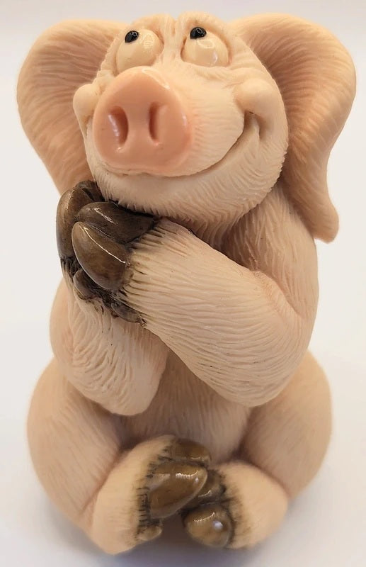 Piggin Romantic figurine by David Corbridge in 1997. A small sculpted pig figurine with a pink snout, beige skin, and dark brown claws, posed sitting with its paws over its mouth against a plain white background.